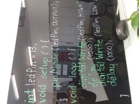 LED code on a whiteboard. It says 'Line 1: int Led Pin equals 13 semi colon. Line 2: void setup open bracket close bracket open curly bracket. Line 3: pin Mode open bracket led Pin comma output close bracket semi colon. Line 4: close curly bracket. Line 5: void loop open bracket close bracket open curly bracket. Line 6: digital write open bracket led pin comma high close bracket. Line 7: delay open bracket 1000 close bracket semi colon. Line 8: digital write open bracket led pin comma low close bracket. Line 9: delay open bracket 1000 close bracket semi colon. Line 10: close curly bracket.